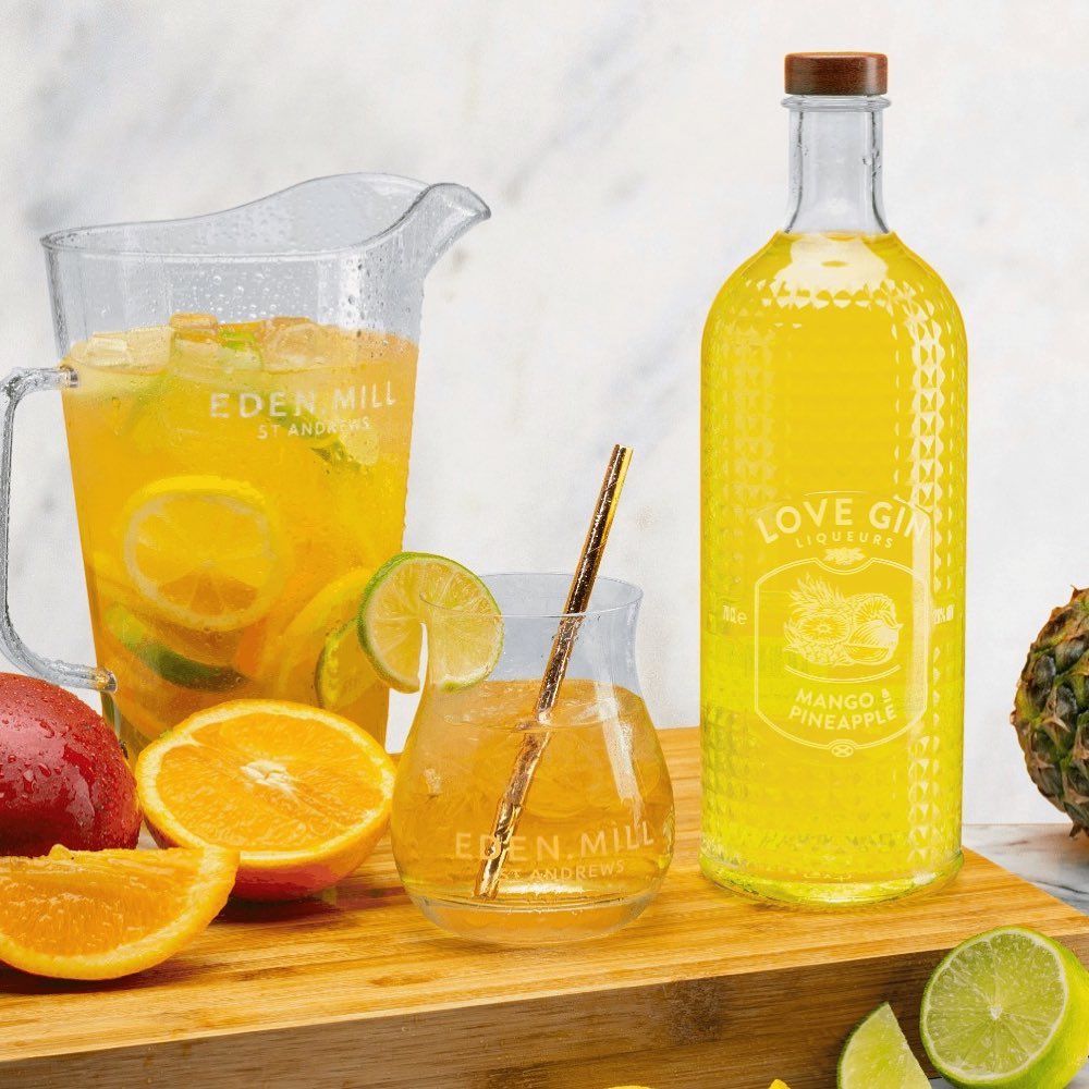 Mango and Pineapple Gin Liqueur Bottle on wooden board with pitcher of cocktail and cut fruit