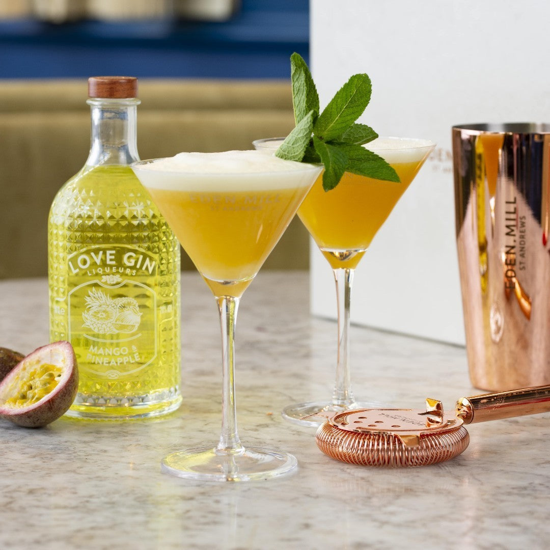 Mango and Pineapple Gin Liqueur Bottle with strainer and two martini glasses with cocktail