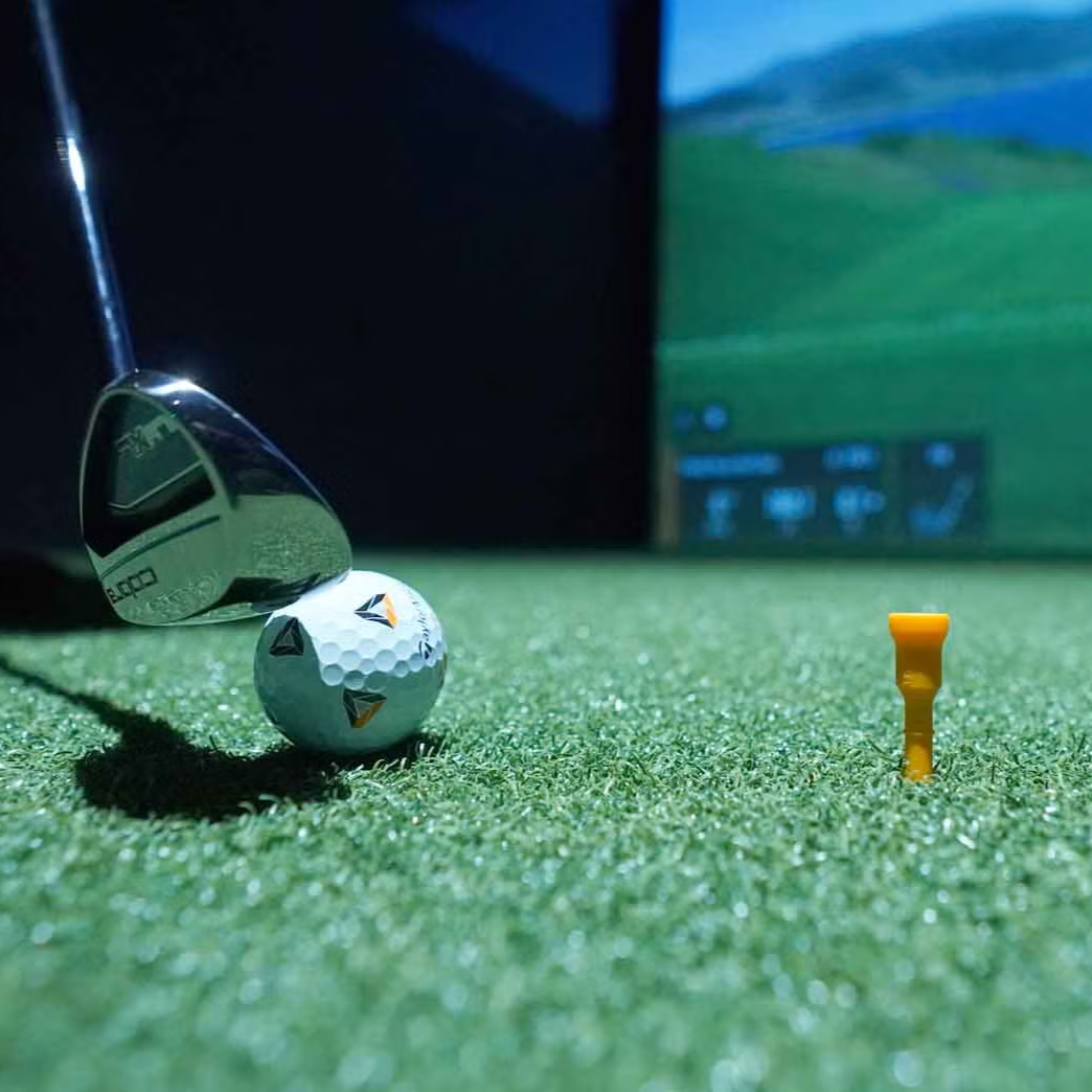 Golf ball, tee, and club on a green surface with a blurred background