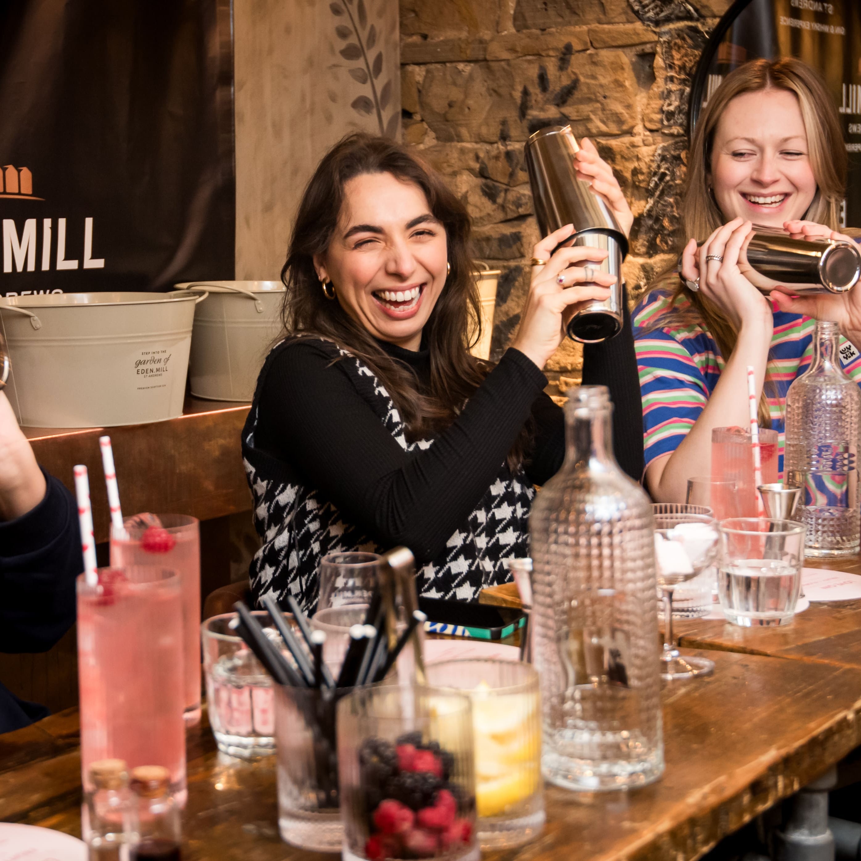 Three women enjoying drinks at a bar with 'Eden Mill' branding in the background.