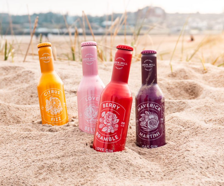 four bottles of eden mill cocktail in different colours in the sand
